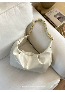 Close-up of beige dumpling bag featuring soft pleated leather and metal chain strap