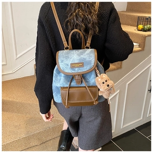 Detail of light blue denim backpack with brown leather trim and cute plush bear charm