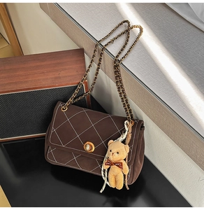Close-up of brown quilted chain bag with a cute bear charm and golden magnetic closure