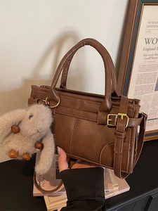 Vintage brown leather handbag with metal buckle and plush rabbit pendant in a cozy setting