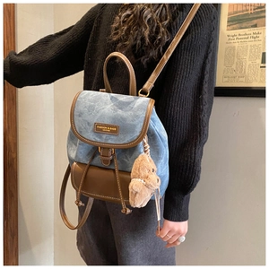 Close-up of blue denim and brown leather backpack with a cute plush bear charm