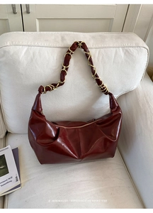 Detail of burgundy glossy leather hobo bag with gold chain strap on soft white sofa
