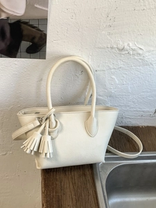 Cream white leather bucket tote bag with dual tassels and adjustable crossbody strap