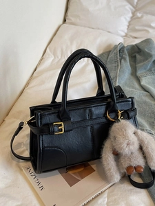 Retro black leather handbag with gold buckle and plush rabbit charm on white bedding