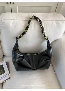 Detail of black crescent shoulder bag with glossy texture and woven gold chain strap