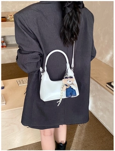 Chic white crescent hobo bag with cute plush bear pendant on a minimalist grey blazer style
