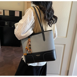 Detail of grey canvas and black leather patchwork tote bag with wooden bead pendant