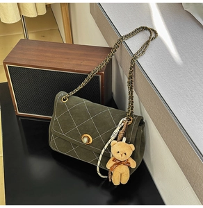 Macro shot of dark green quilted suede handbag featuring a vintage gold clasp and bear charm