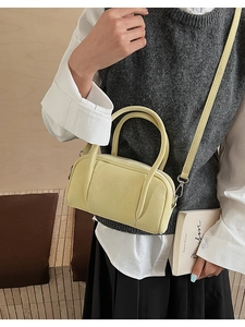 Detailed view of creamy yellow Boston bag with smooth top handles and crossbody strap