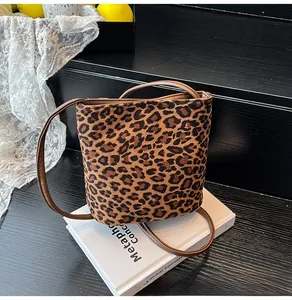 Détail du sac seau en toile à motif léopard avec bandoulière en cuir marron sur un livre
