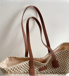 Detail of straw woven tote bag featuring brown leather straps and smooth beige interior lining