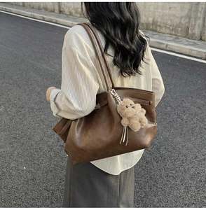 Detail of vintage brown leather tote bag with pleated texture and cute plush bear charm