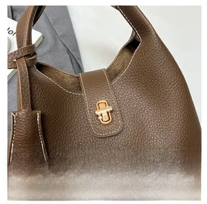 Close-up of brown litchi grain leather handbag with gold rotating lock and white stitching