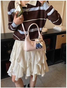 Pink patent leather dumpling bag with teddy bear pendant shown on model in polo shirt
