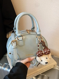 Light blue Boston style handbag with bear charm on a silver suitcase background