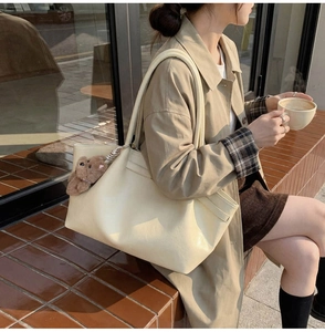 Close-up of cream leather tote bag with a cute brown bear charm on the strap