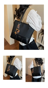 Detail of black leather tote bag with white stitching and decorative wooden beads