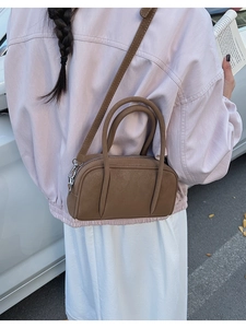 Detail of a dark brown leather crossbody bag held by a model in a casual outfit