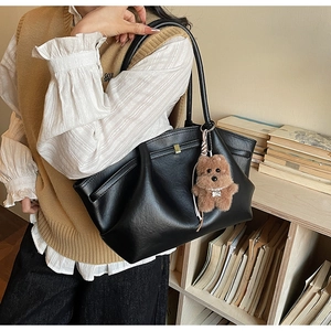Detail of black pleated tote bag with golden buckle and brown teddy bear charm accessory