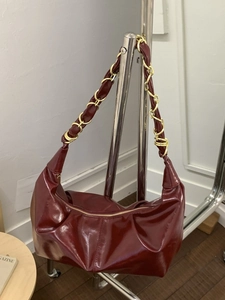 Burgundy glossy hobo bag with a stylish gold chain strap displayed on a stand