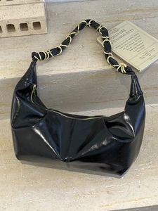 Glossy black crescent shoulder bag with a woven gold chain strap on marble steps