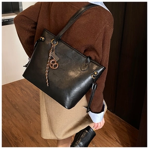 Detail of black glossy tote bag featuring a brown butterfly charm and metallic ring accents