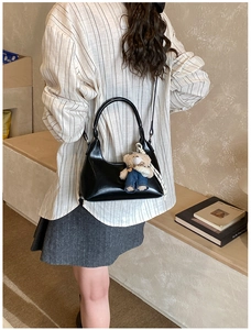 Detail of black glossy faux leather hobo bag with a cute plush bear pendant accessory
