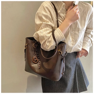 Detail of dark brown leather tote bag with wooden charm and adjustable metal buckle