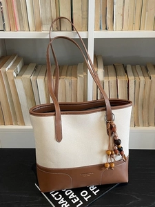 Retro canvas and brown leather tote bag with wooden bead charm on a book-lined background