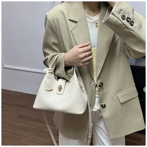 Close-up of beige lychee leather trapezoid bucket bag with gold metal clasp on a model