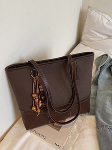 Brown canvas patchwork tote bag with white stitching and wood bead charm on bed