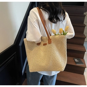 Detail of beige hollow woven straw tote bag with brown leather straps worn by a model