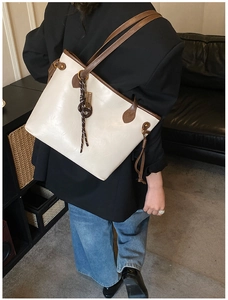 Detail of cream white faux leather tote bag with brown straps and tassel charm shown on model