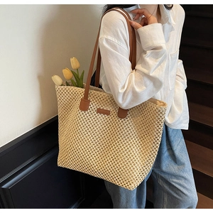 Detailed close-up of woven straw tote bag with brown leather handles and brand tag