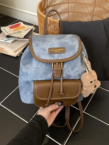 Retro denim backpack with leather trim and bear pendant for women in a stylish setting