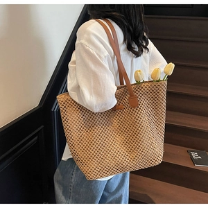 Detail of hollow mesh woven straw tote bag with brown leather straps on model