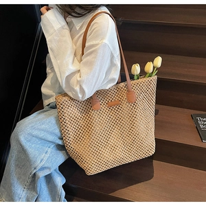 Detail of woven straw tote bag featuring brown leather handles and rustic mesh texture