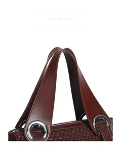 Detail of burgundy woven shoulder bag featuring thick curved handles and silver metal rings