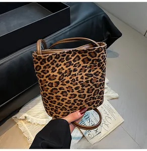 Gros plan sur un sac seau à imprimé léopard avec poignée marron tenu par un mannequin en scène
