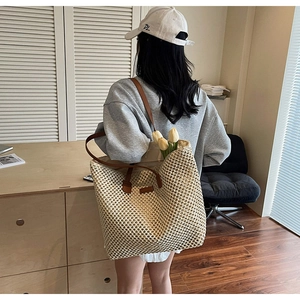 Detail of a beige straw tote bag with brown leather handles worn over the shoulder