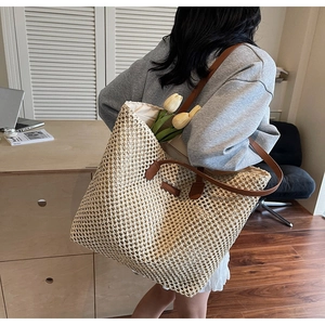 Detail of hand-woven straw tote bag with brown leather handles and textured grid pattern