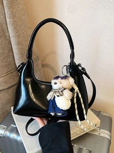 Chic black glossy crescent moon hobo bag with teddy bear charm on stack of books
