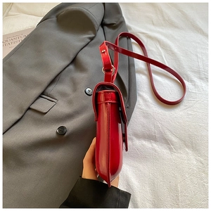 Detail view of red glossy patent leather handbag on white fabric and grey suit background