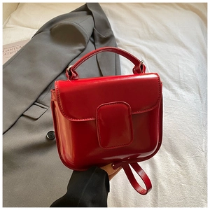 Detail of red patent leather mini handbag with top handle and matching shoulder strap