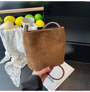 Détail d'un sac seau en daim marron mat avec poignée ronde et bandoulière fine