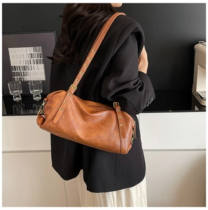 Detail of a vintage brown leather bag with metallic rivets and adjustable strap on a model