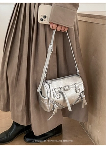 Close-up of metallic silver shoulder bag featuring decorative zippers and buckles