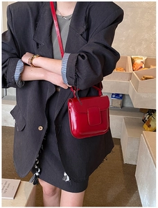 Red oil wax leather crossbody bag worn over a dark blazer in a cozy cafe setting