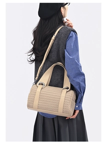 Detail view of beige woven cylinder pillow bag on model with blue plaid shirt