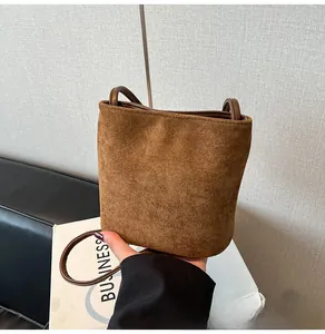Détail d'un sac seau en daim marron avec de fines anses en cuir et design minimaliste